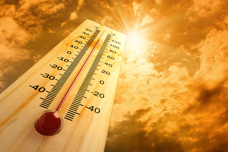 A thermometer showing a high temperature against an orange sky with the sun shining brightly through clouds, conveying intense heat.