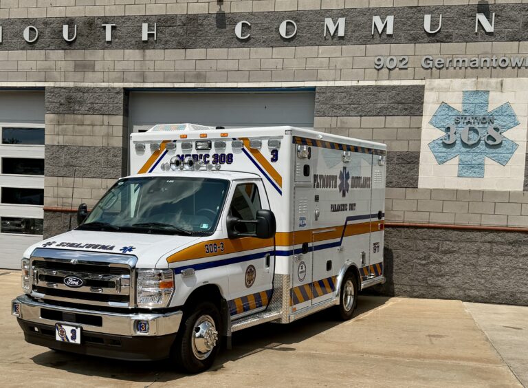 A Plymouth Ambulance vehicle is parked in front of a building with "Station 308" and "902 Germantown" visible on the wall. The ambulance has blue and yellow stripes and emergency markings.
