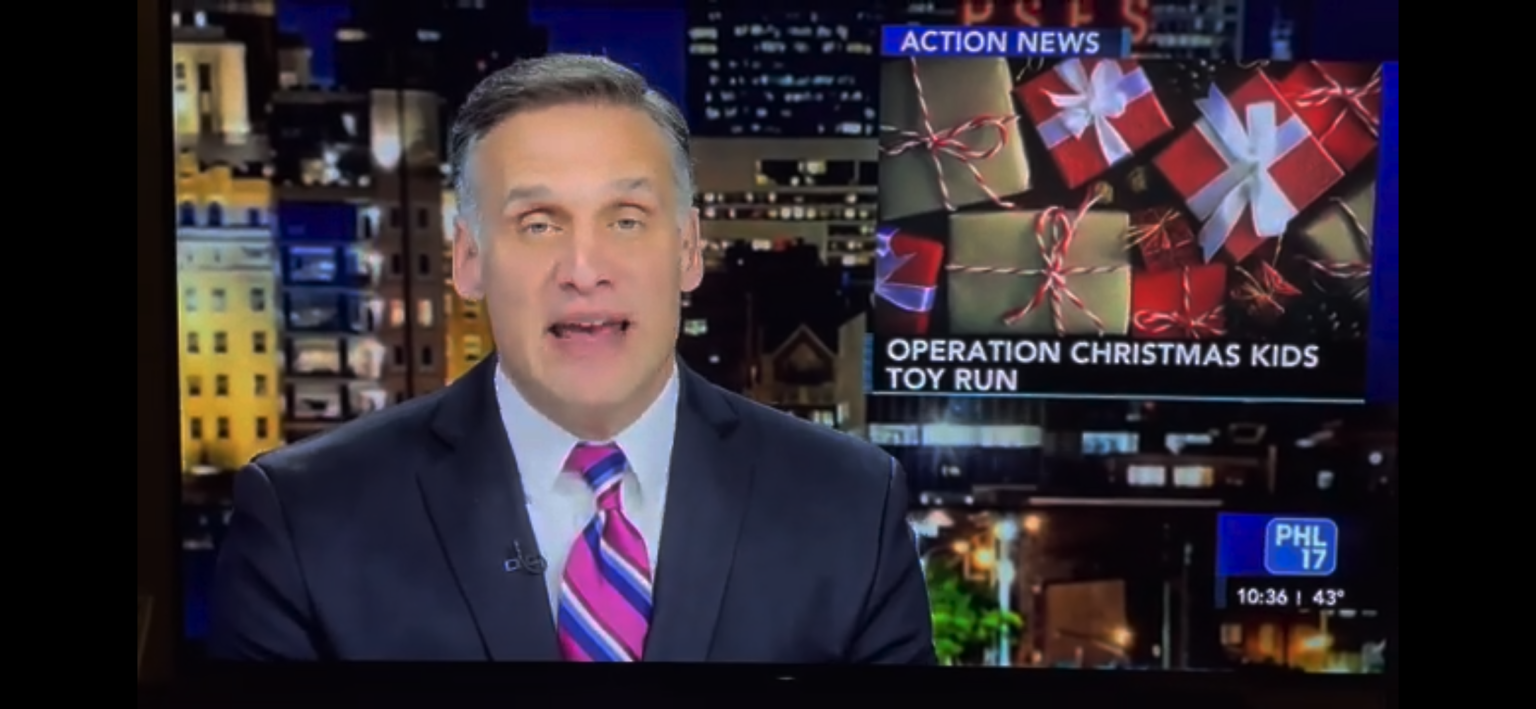 A male news anchor in a suit and striped tie reports on "Operation Christmas Kids Toy Run" with an image of wrapped gifts on the screen. The broadcast is from PHL 17, and the time is 10:26 with a temperature of 43°F.