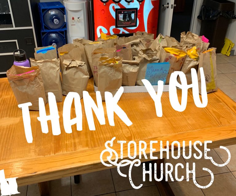 A wooden table with brown paper lunch bags, some with colorful handles, has the words “THANK YOU” and “STOREHOUSE CHURCH” written over the image in bold white text. A drink machine and water jugs are in the background.
